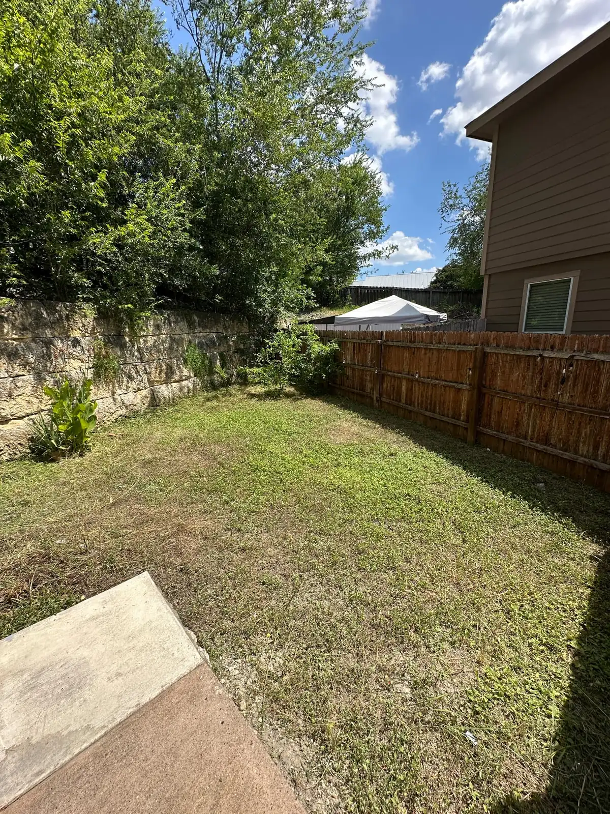 The same residential backyard freshly mowed, trimmed along the fence line, and cleaned up after lawn maintenance service.