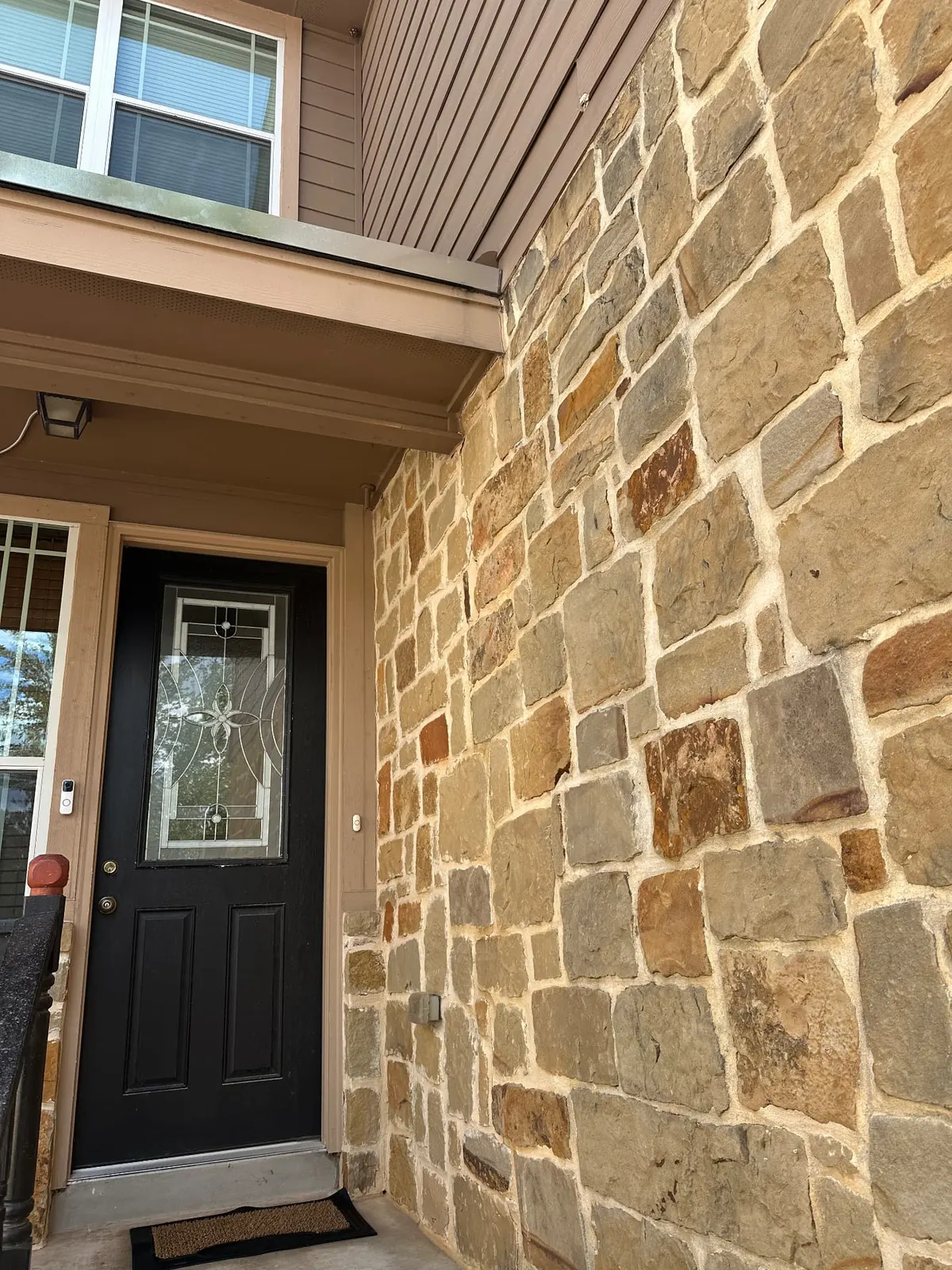 The same doorway and stone wall after pressure washing, with clean mortar joints and porch.