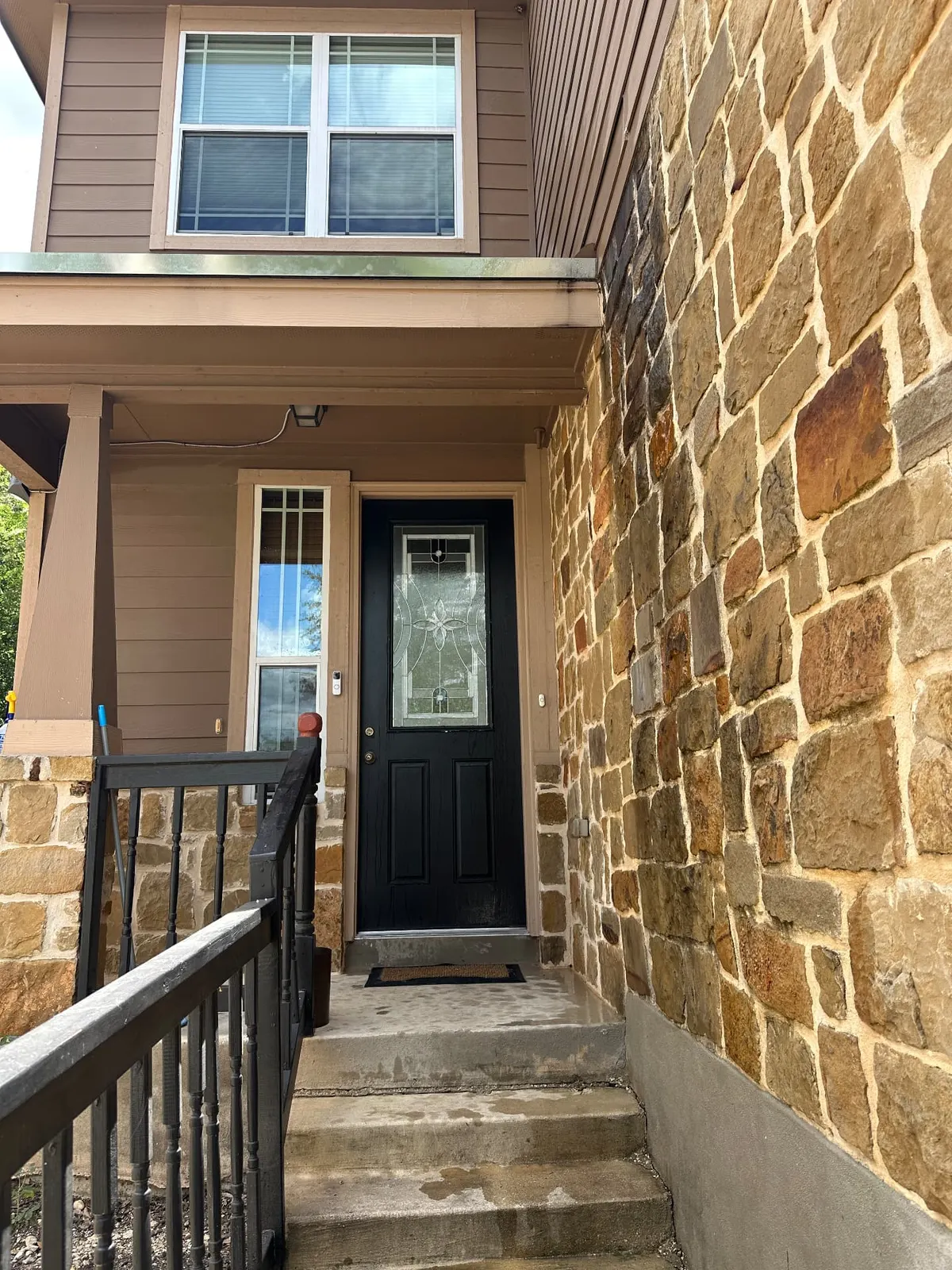 Front entryway with dull, dirty stone veneer and stained concrete steps before pressure washing.