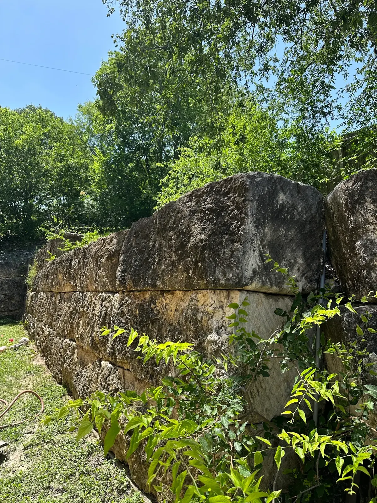 Corner section of the block retaining wall with dark staining and moss growth before pressure washing.