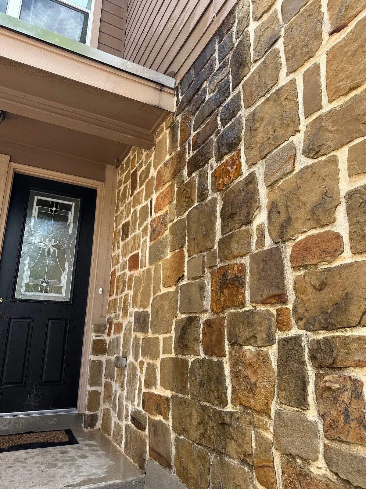 Close view of the front door, porch, and stone wall with dirt and buildup before pressure washing.
